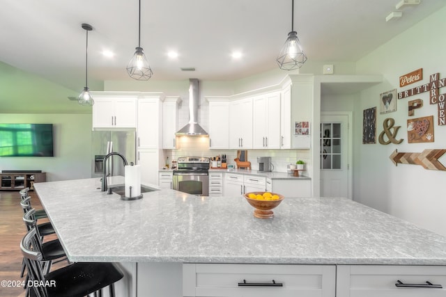 kitchen featuring stainless steel appliances, wall chimney exhaust hood, a sink, a large island, and white cabinetry