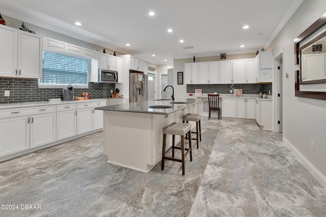 kitchen featuring white cabinetry, appliances with stainless steel finishes, decorative backsplash, and a center island with sink