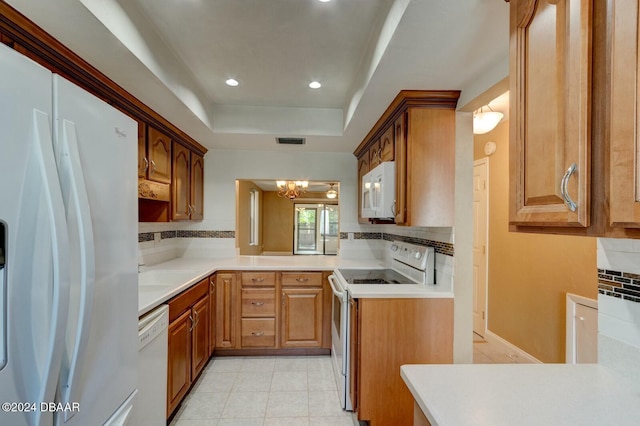 kitchen with an inviting chandelier, a raised ceiling, backsplash, white appliances, and light tile patterned floors