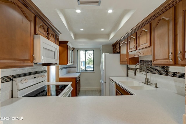 kitchen with a tray ceiling, decorative backsplash, sink, and white appliances