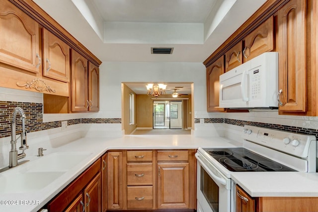 kitchen with white appliances, ceiling fan with notable chandelier, a raised ceiling, sink, and tasteful backsplash