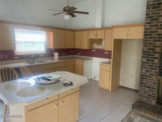 kitchen featuring light tile patterned floors, a ceiling fan, a kitchen island, a sink, and light countertops