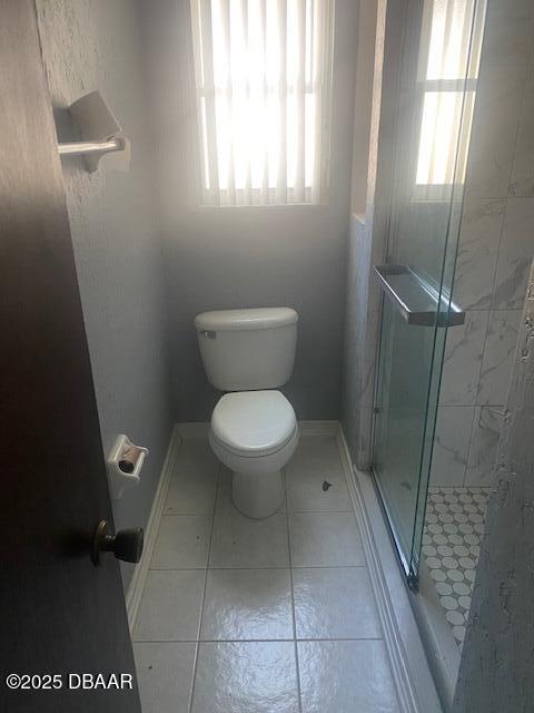 bathroom featuring tile patterned floors, a stall shower, toilet, and baseboards