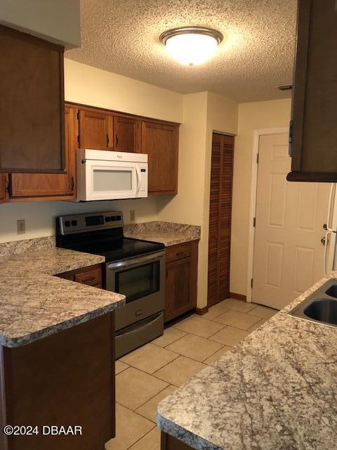 kitchen with light tile patterned flooring, a textured ceiling, stainless steel range with electric stovetop, and sink