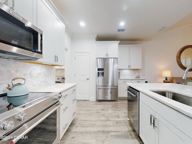 kitchen featuring sink, white cabinets, high end appliances, light hardwood / wood-style floors, and crown molding