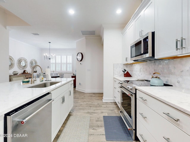 kitchen with sink, white cabinetry, light stone counters, appliances with stainless steel finishes, and pendant lighting