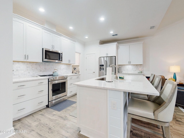 kitchen with light hardwood / wood-style flooring, ornamental molding, a kitchen breakfast bar, stainless steel appliances, and white cabinets