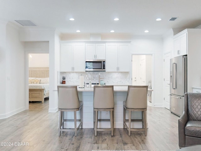 kitchen with appliances with stainless steel finishes, a breakfast bar, a kitchen island with sink, and white cabinets