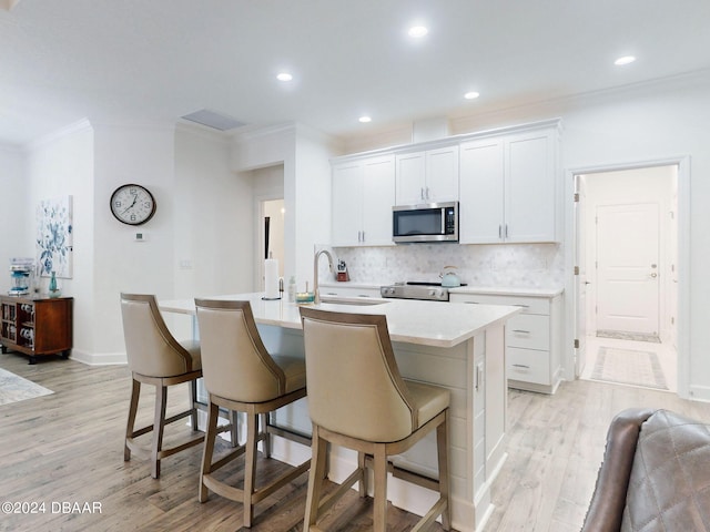 kitchen with appliances with stainless steel finishes, a breakfast bar, a center island with sink, and white cabinets