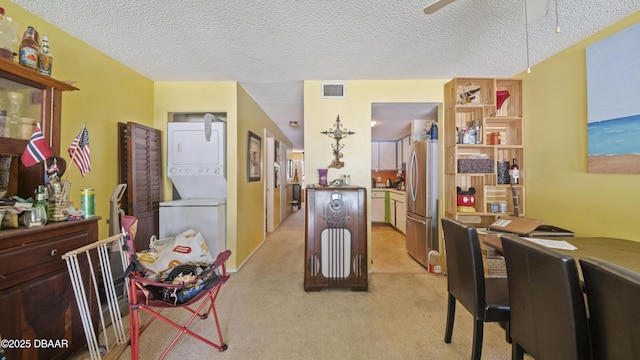 kitchen featuring ceiling fan, stacked washer and dryer, light colored carpet, visible vents, and freestanding refrigerator