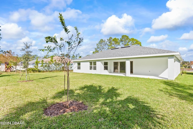 back of property featuring a yard, a shingled roof, and stucco siding