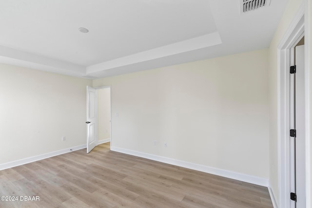 spare room featuring light wood finished floors, baseboards, and a raised ceiling