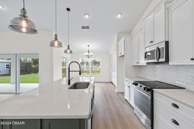 kitchen featuring stainless steel microwave, electric range, a sink, tasteful backsplash, and an island with sink