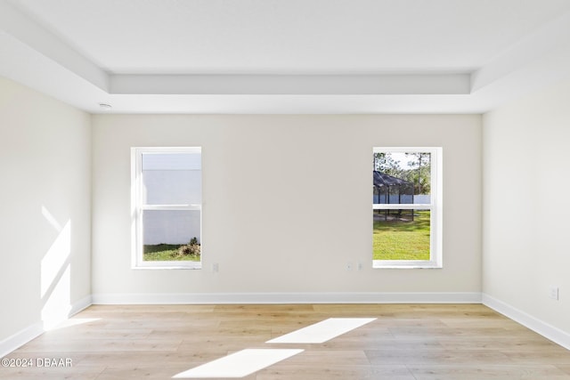 empty room with light wood-style floors, a tray ceiling, and baseboards