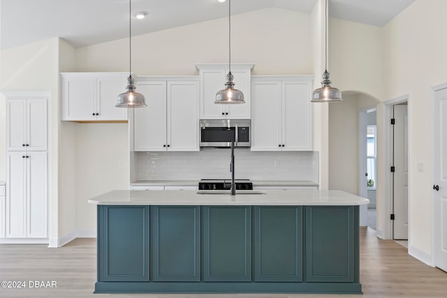 kitchen featuring stainless steel microwave, white cabinetry, decorative backsplash, light wood-style flooring, and high vaulted ceiling