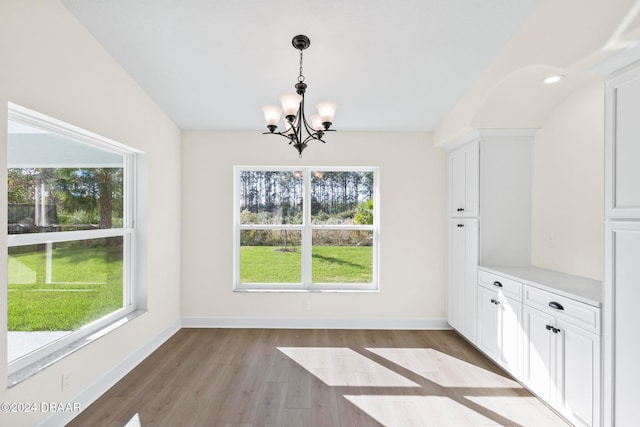 unfurnished dining area featuring a chandelier, light wood-style flooring, and baseboards