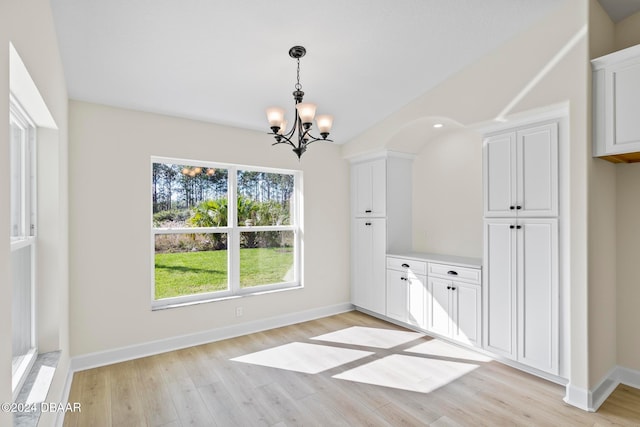 unfurnished dining area with a chandelier, light wood-style flooring, and baseboards