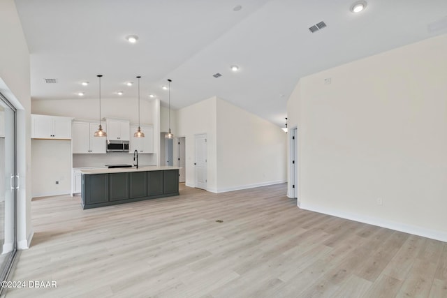 kitchen featuring open floor plan, stainless steel microwave, white cabinets, light countertops, and a sink