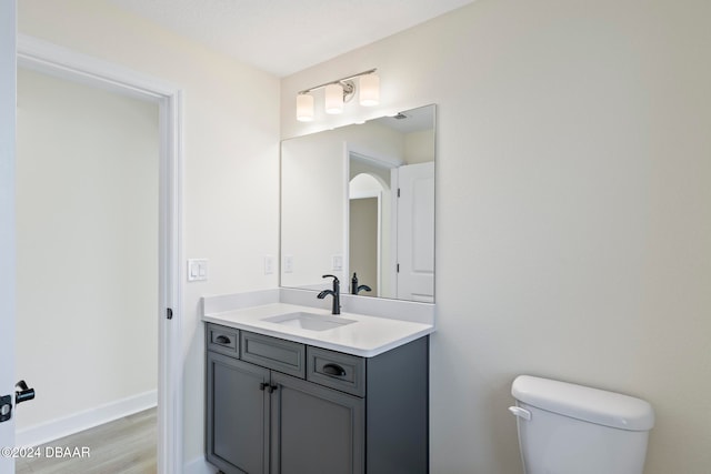 bathroom with toilet, vanity, wood finished floors, and baseboards