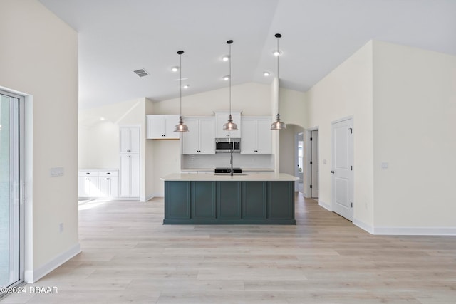 kitchen featuring white cabinetry, stainless steel microwave, high vaulted ceiling, light countertops, and light wood-style flooring
