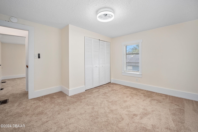 unfurnished bedroom featuring light colored carpet, a textured ceiling, and a closet