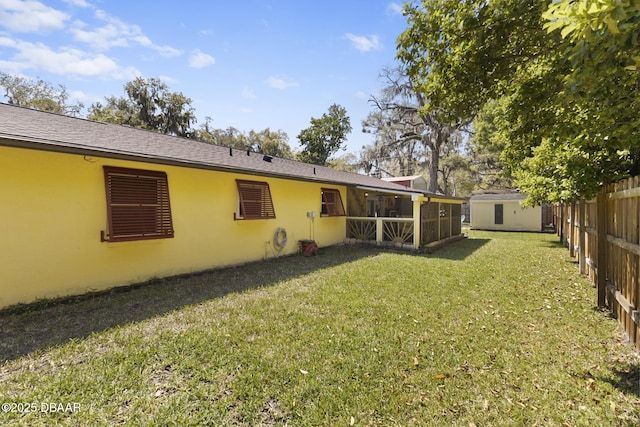 rear view of house featuring stucco siding, a lawn, an outdoor structure, and fence