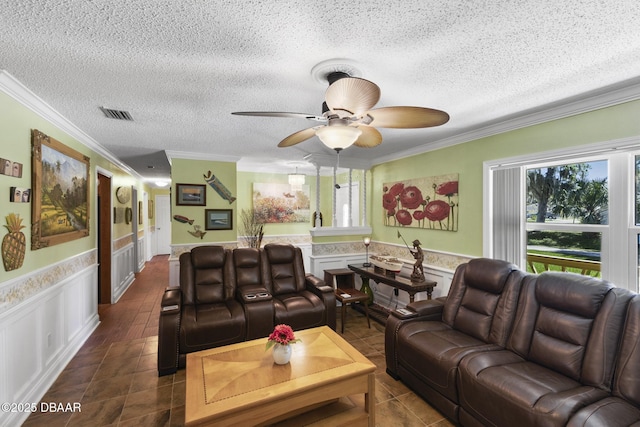 living room featuring a wainscoted wall, dark tile patterned flooring, ceiling fan, ornamental molding, and a textured ceiling