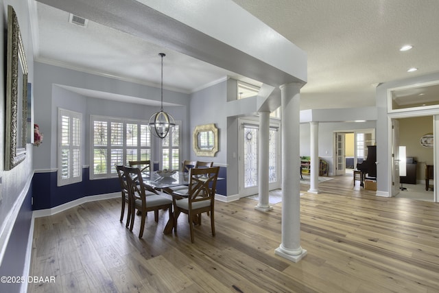 dining area with an inviting chandelier, ornamental molding, wood-type flooring, and decorative columns