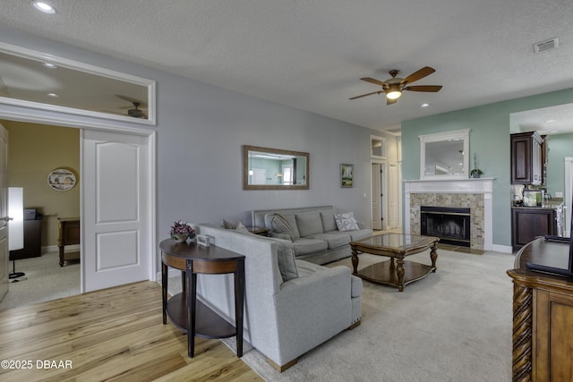 living room with a tile fireplace, a textured ceiling, ceiling fan, and light hardwood / wood-style flooring