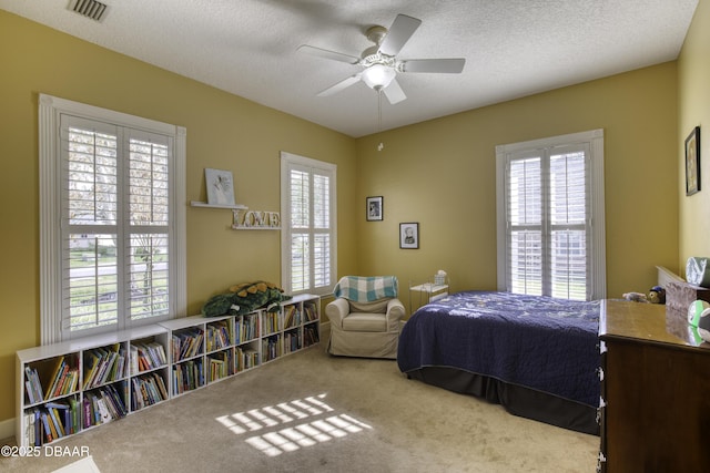 carpeted bedroom featuring ceiling fan, multiple windows, and a textured ceiling