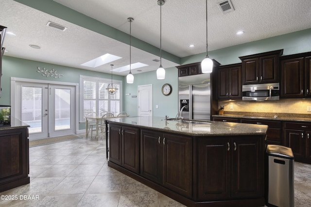 kitchen featuring decorative light fixtures, sink, stainless steel appliances, dark brown cabinets, and a center island with sink