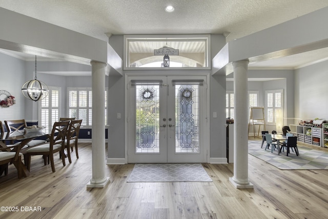 entrance foyer with ornate columns, a chandelier, a healthy amount of sunlight, light wood-type flooring, and french doors