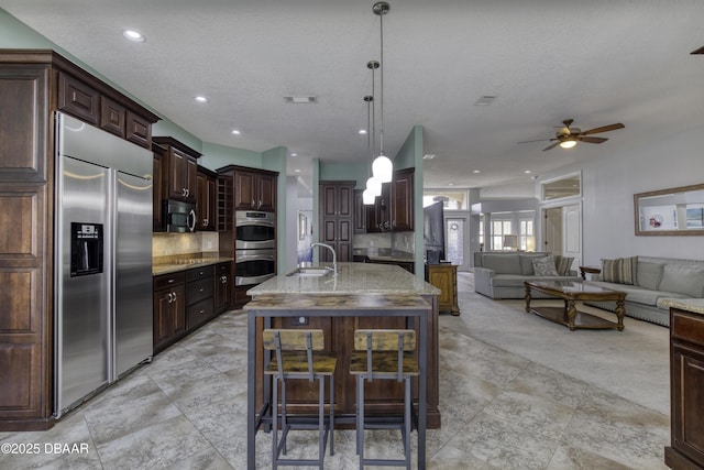 kitchen with dark brown cabinetry, a breakfast bar area, hanging light fixtures, a center island with sink, and stainless steel appliances