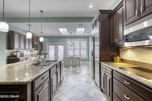 kitchen with appliances with stainless steel finishes, a kitchen island with sink, dark brown cabinets, and decorative light fixtures