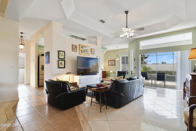 tiled living room with a tray ceiling, ceiling fan, and a towering ceiling