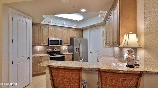 kitchen with kitchen peninsula, a raised ceiling, appliances with stainless steel finishes, backsplash, and a kitchen bar