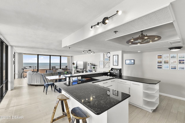 kitchen featuring white cabinets, expansive windows, kitchen peninsula, a breakfast bar, and a water view