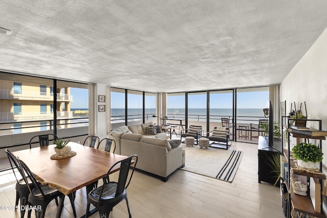 interior space with a view of the beach, light wood-type flooring, a water view, and a wall of windows