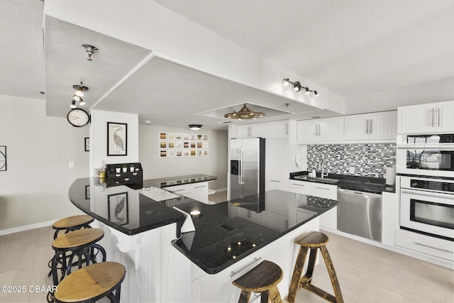 kitchen featuring kitchen peninsula, a breakfast bar, stainless steel appliances, sink, and white cabinetry