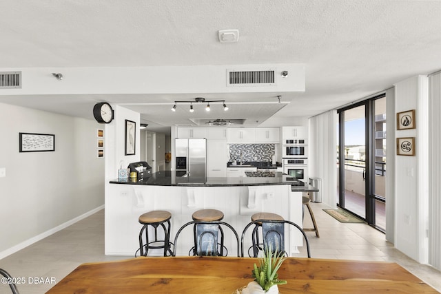 kitchen with expansive windows, stainless steel refrigerator with ice dispenser, kitchen peninsula, decorative backsplash, and white cabinetry