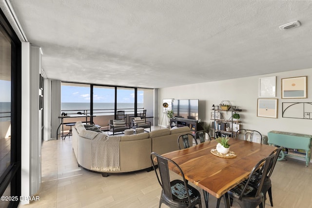 dining room featuring expansive windows, a water view, and a textured ceiling