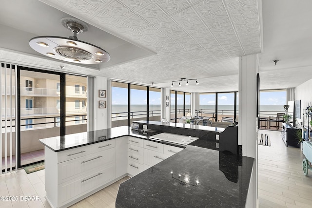 kitchen featuring kitchen peninsula, white cabinetry, a wall of windows, and dark stone countertops