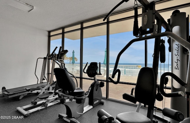 workout area with floor to ceiling windows, a water view, and a textured ceiling