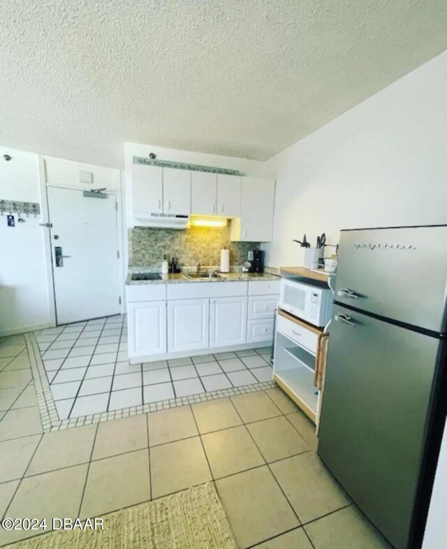 kitchen with stainless steel refrigerator, light tile patterned flooring, and white cabinets