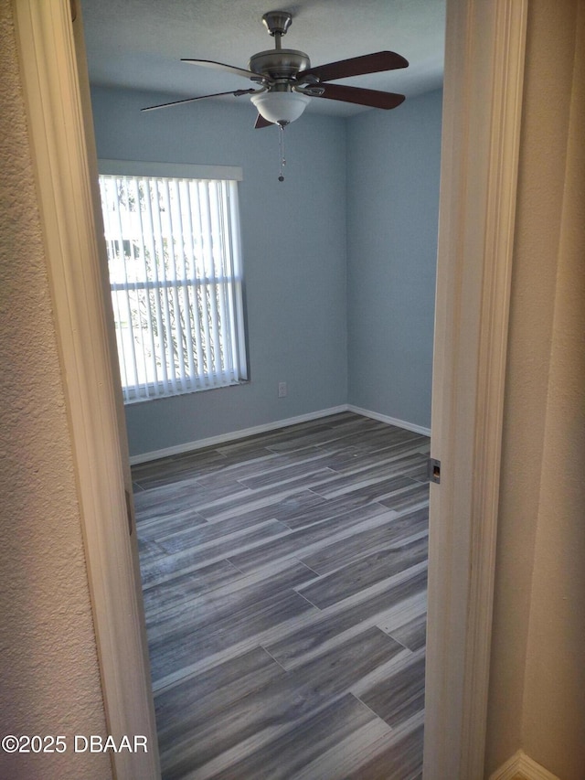 unfurnished room featuring ceiling fan, baseboards, and dark wood finished floors