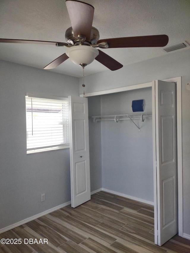 unfurnished bedroom featuring visible vents, ceiling fan, baseboards, wood finished floors, and a closet