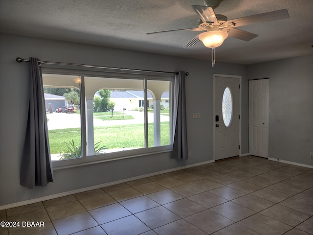 tiled foyer featuring baseboards, a textured ceiling, and a ceiling fan