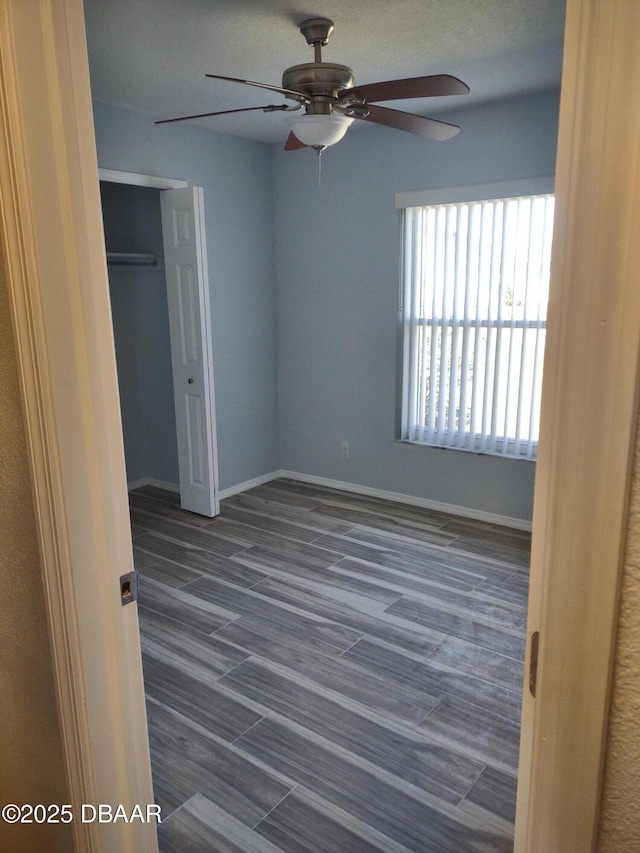 unfurnished bedroom featuring a closet, baseboards, dark wood-style floors, and a ceiling fan