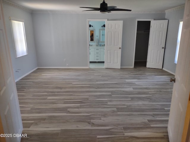 unfurnished bedroom with baseboards, ornamental molding, ensuite bathroom, wood finished floors, and a closet