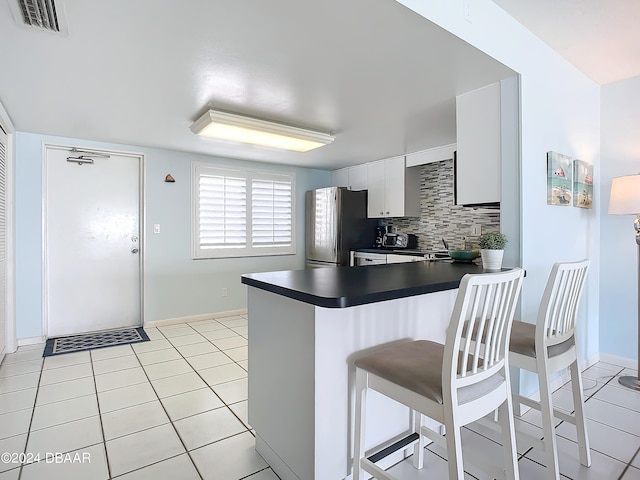 kitchen featuring white cabinets, stainless steel refrigerator, kitchen peninsula, and tasteful backsplash